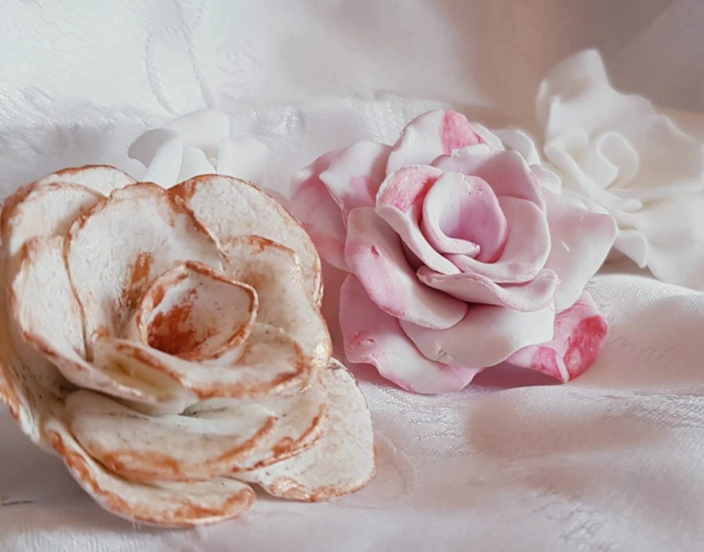 Three roses made with white chocolate modelling chocolate. One with gold edges, one pink and white marbled and one white. 