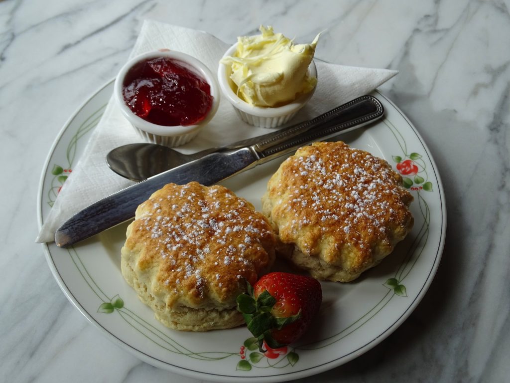 two buttermilk scones served with clotted cream , jam and a strawberry.

